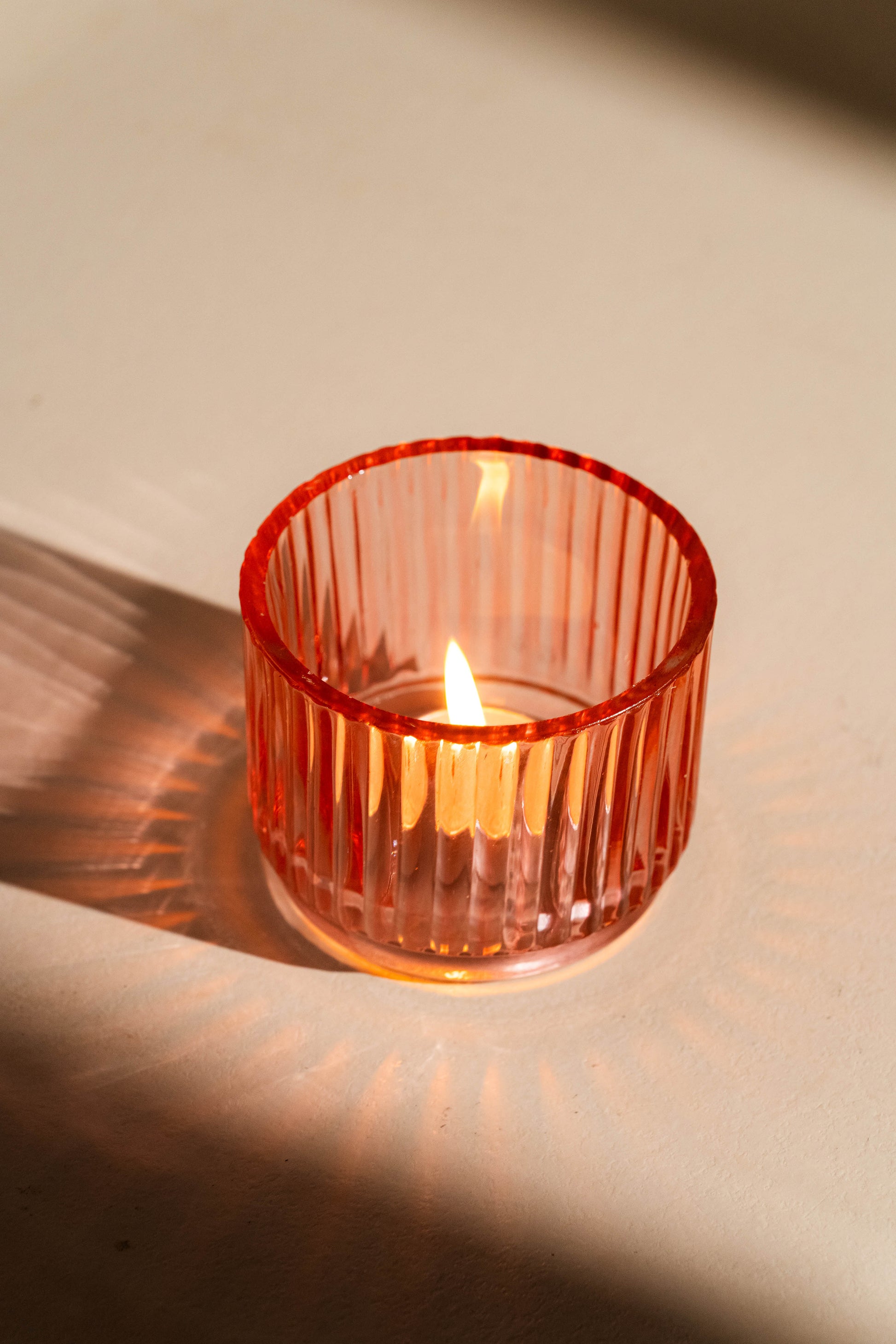 Lit candle in a ribbed red glass holder on a neutral background