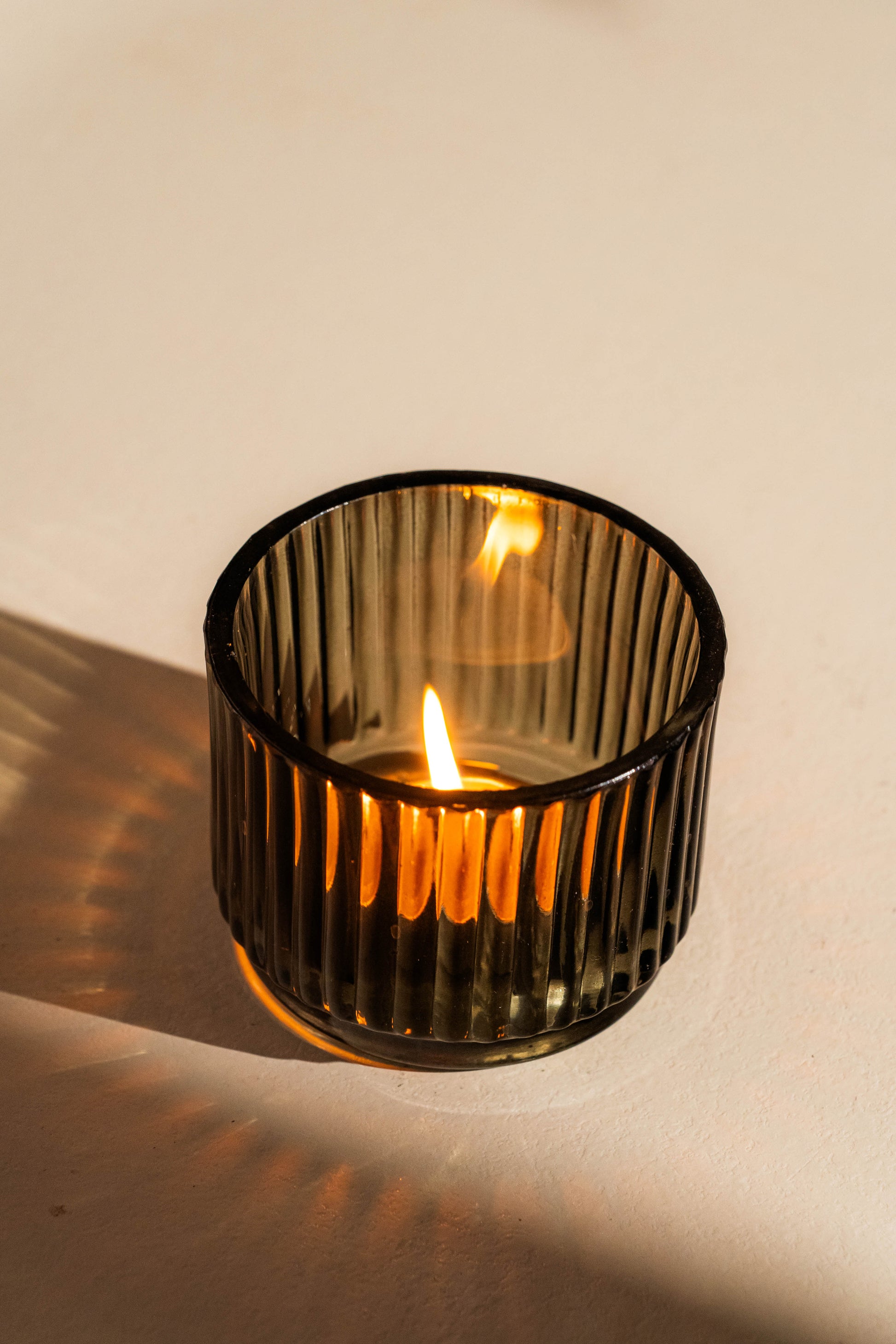 Candle in a ribbed glass holder on a beige background