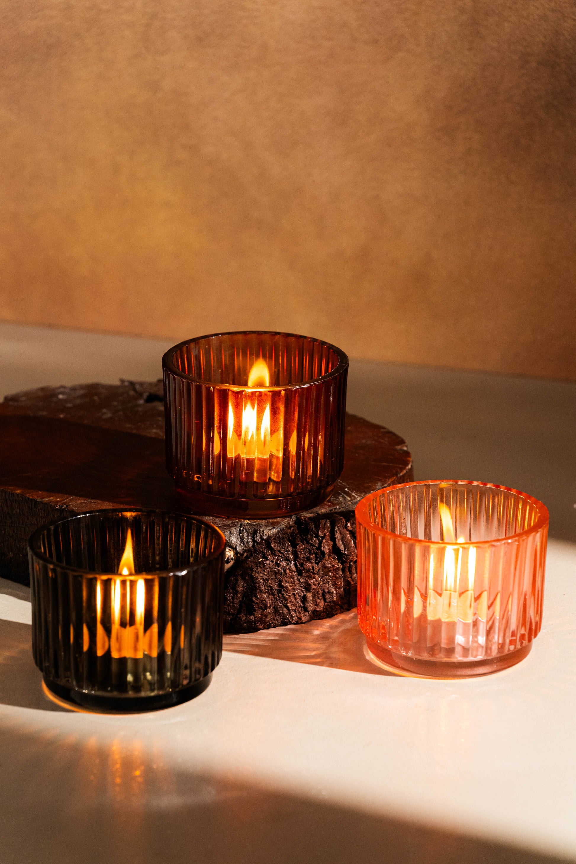 Three lit candles in glass holders on a wooden surface with a warm background