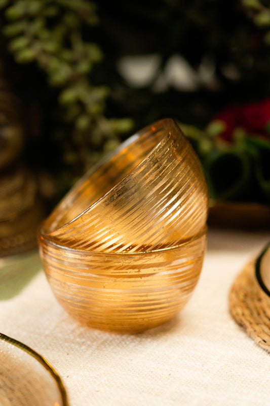 Stack of gold textured bowls on a light surface with blurred greenery in the background
