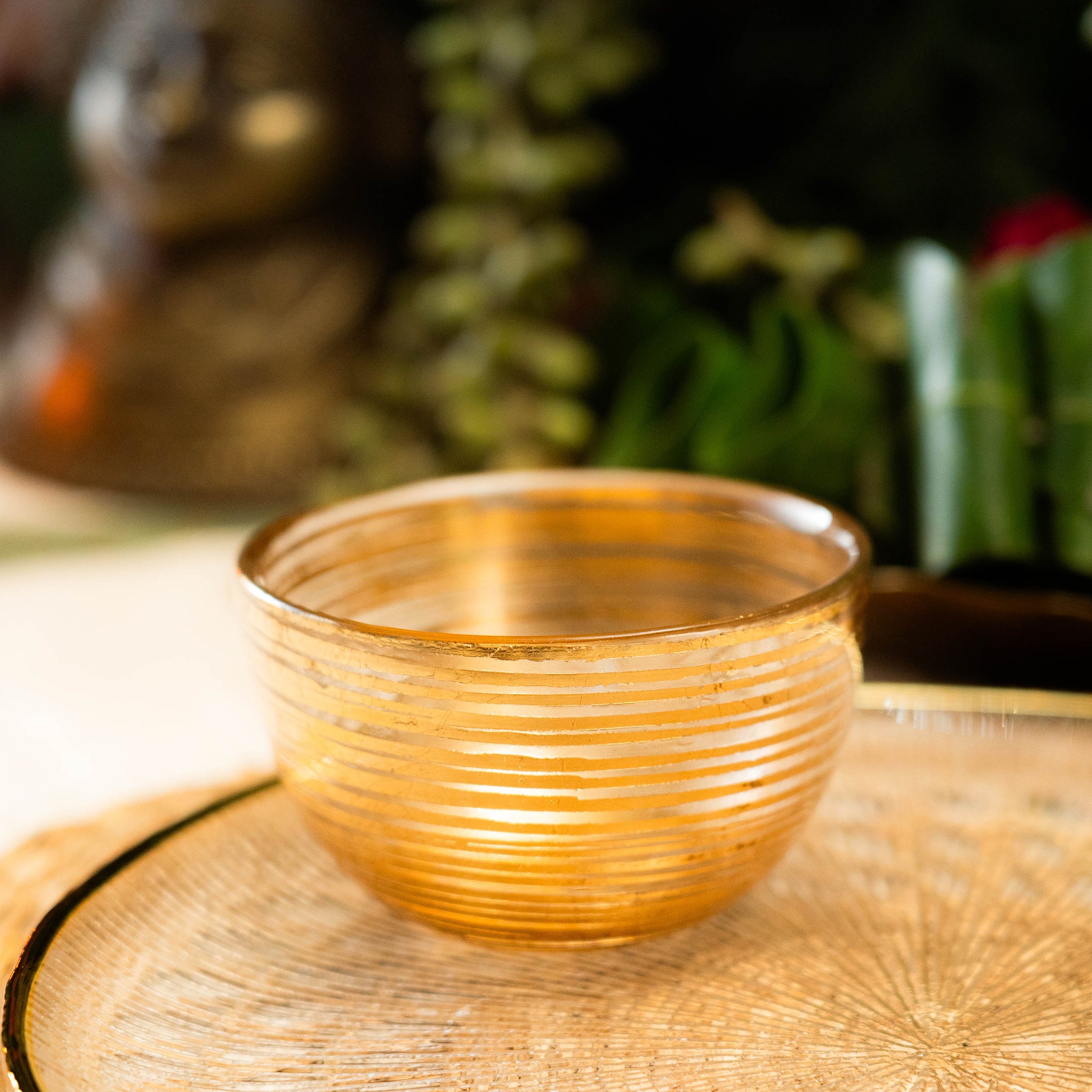 Gold glass bowl on a textured surface with blurred greenery in the background