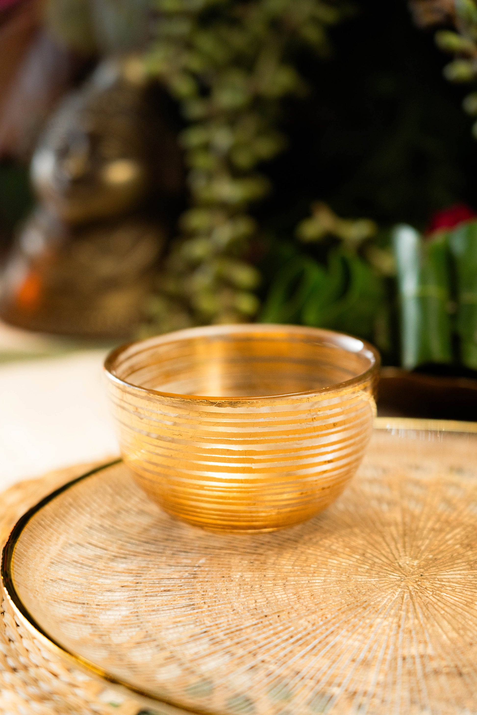 Gold glass bowl on a textured surface with blurred greenery in the background