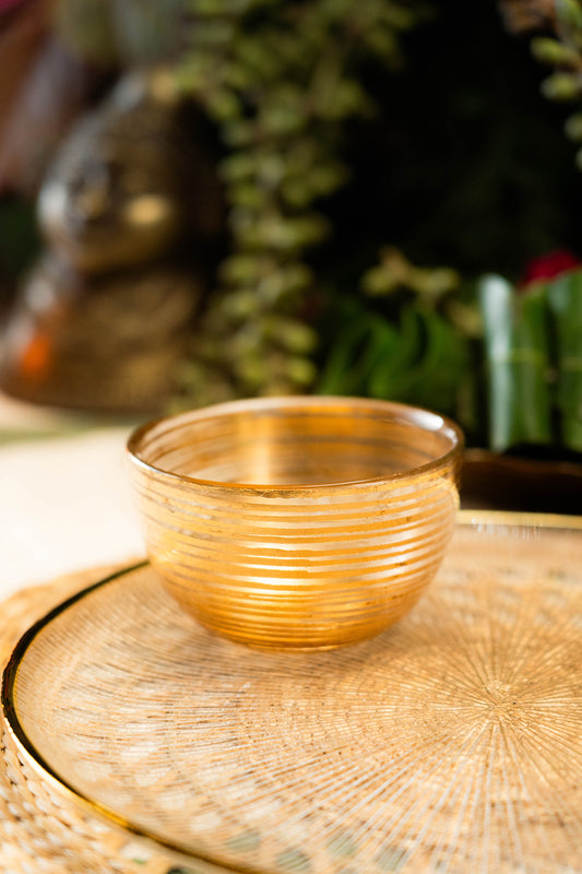 Gold glass bowl on a textured surface with blurred greenery in the background