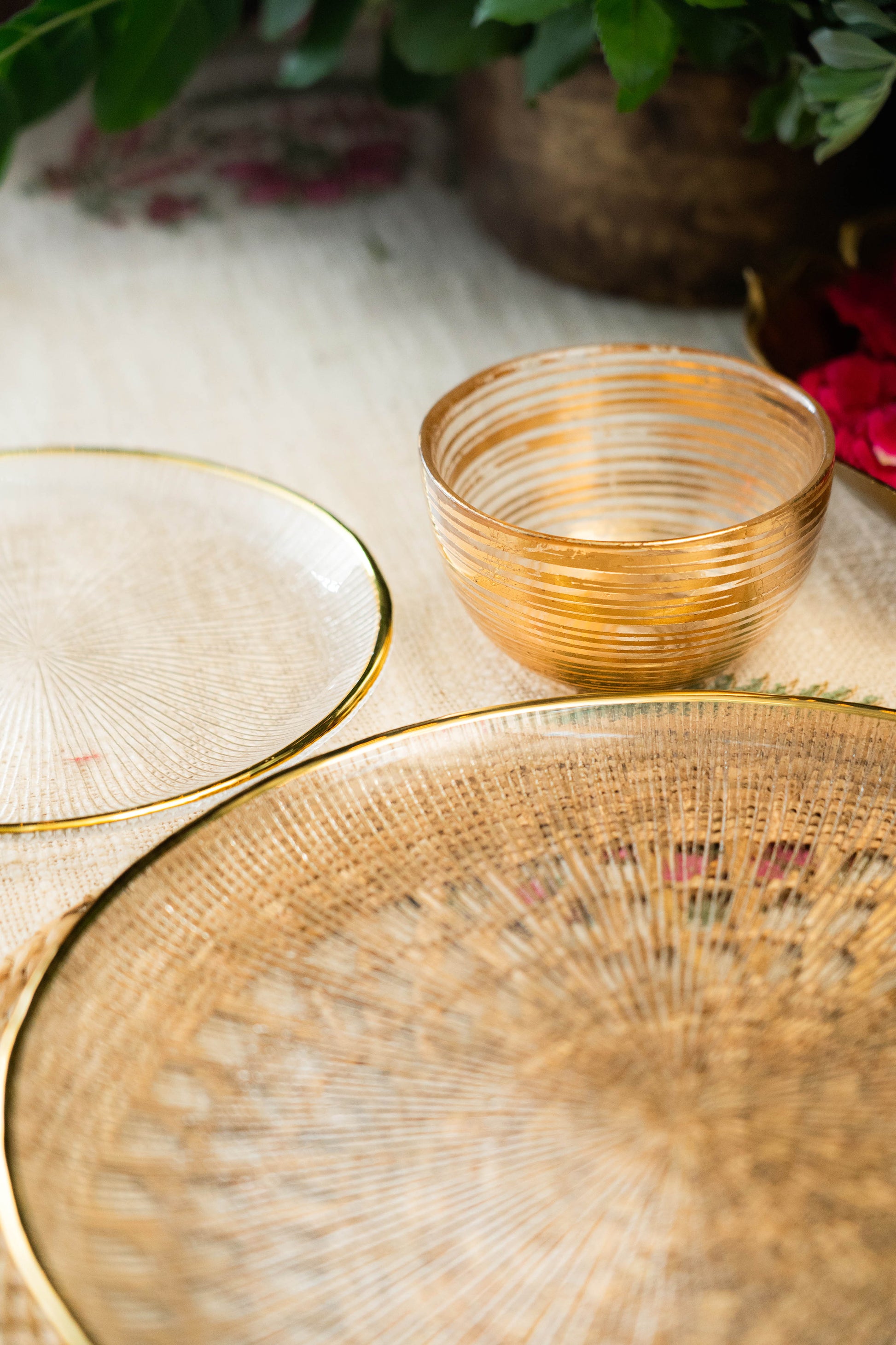 Gold glass bowls and a woven basket on a light surface with blurred greenery in the background.