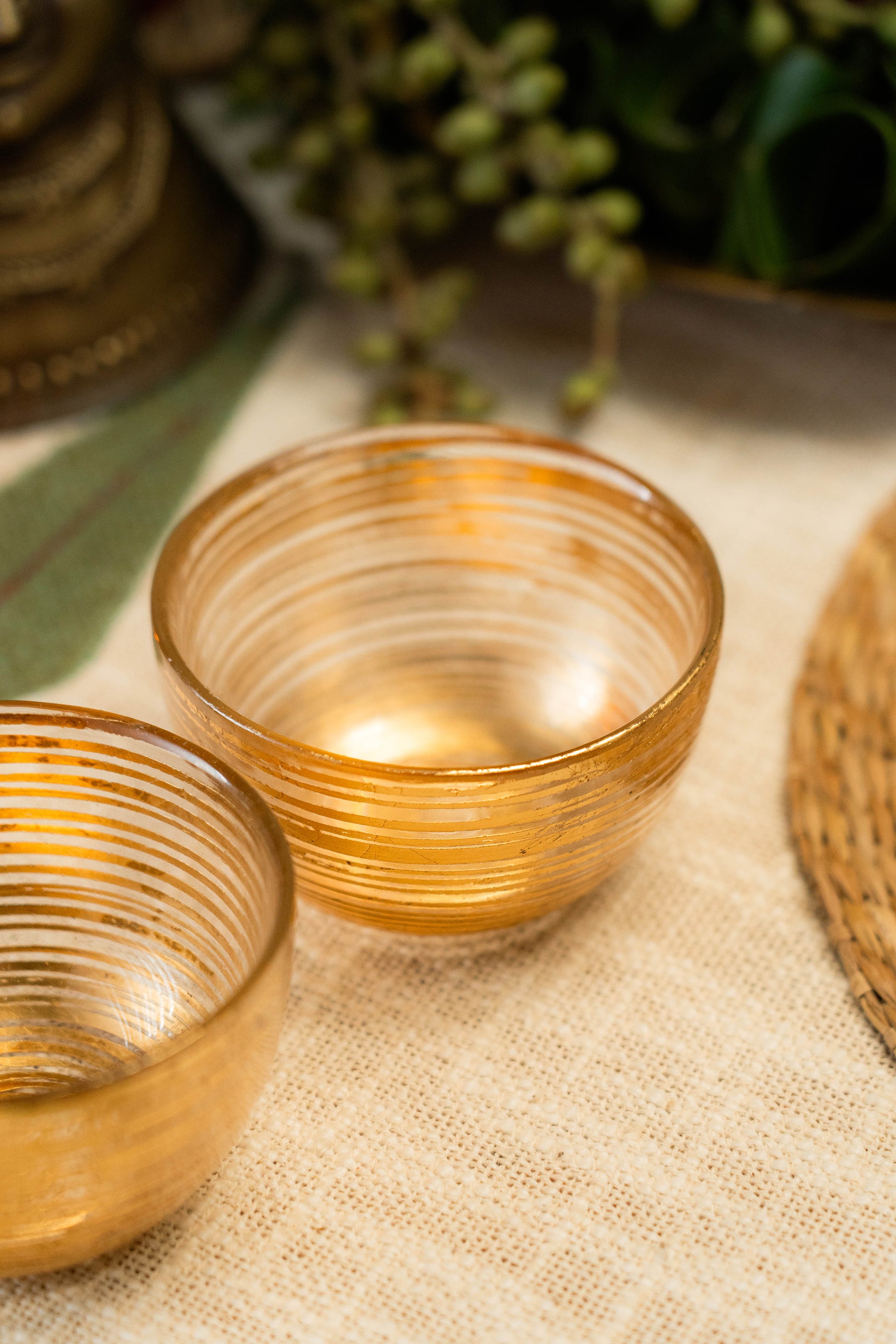 Two gold-rimmed glass bowls on a textured surface with greenery in the background