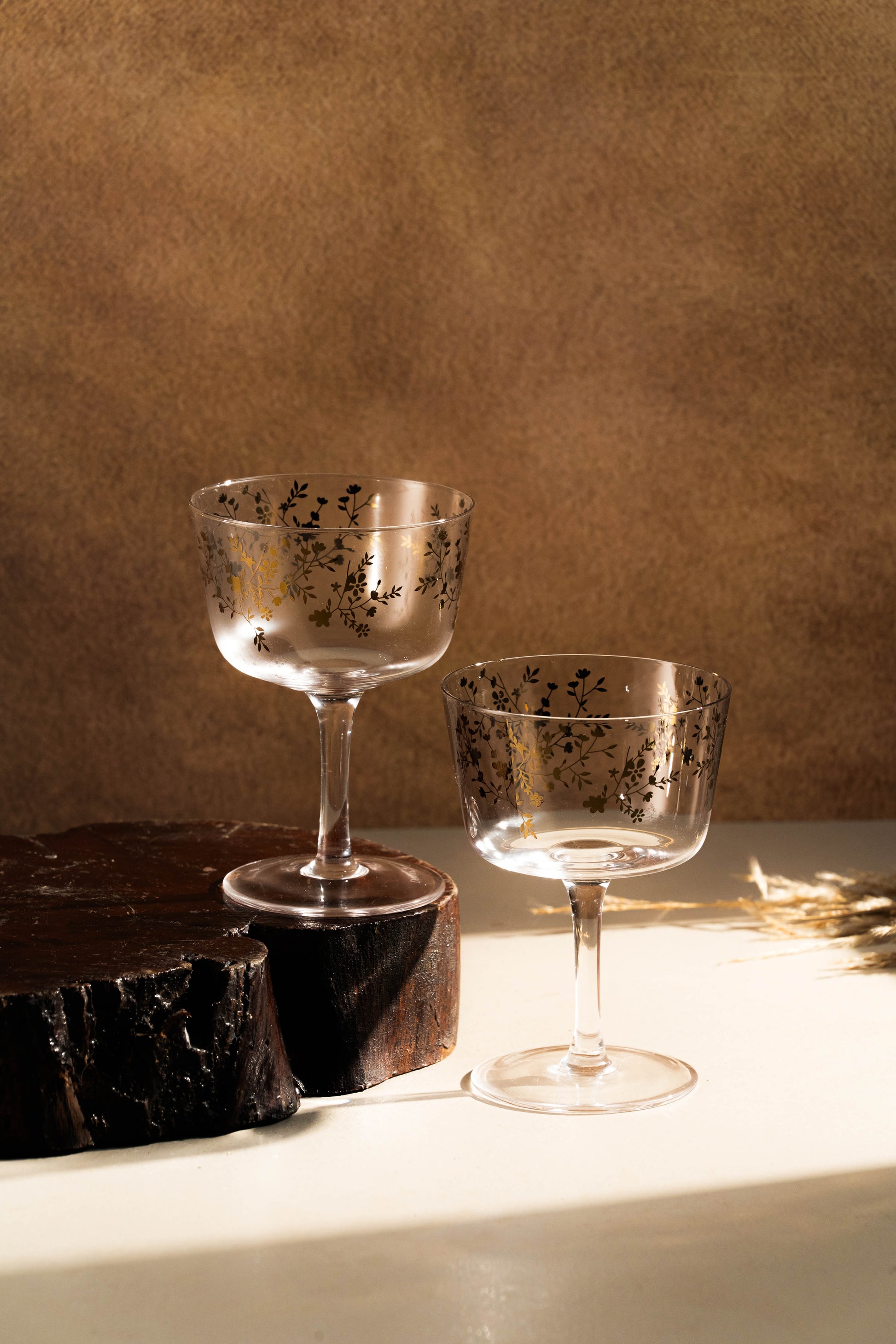 Two decorative glasses on a wooden surface with a brown background