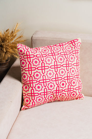 Pink and white patterned pillow on a beige couch with a plant in the background