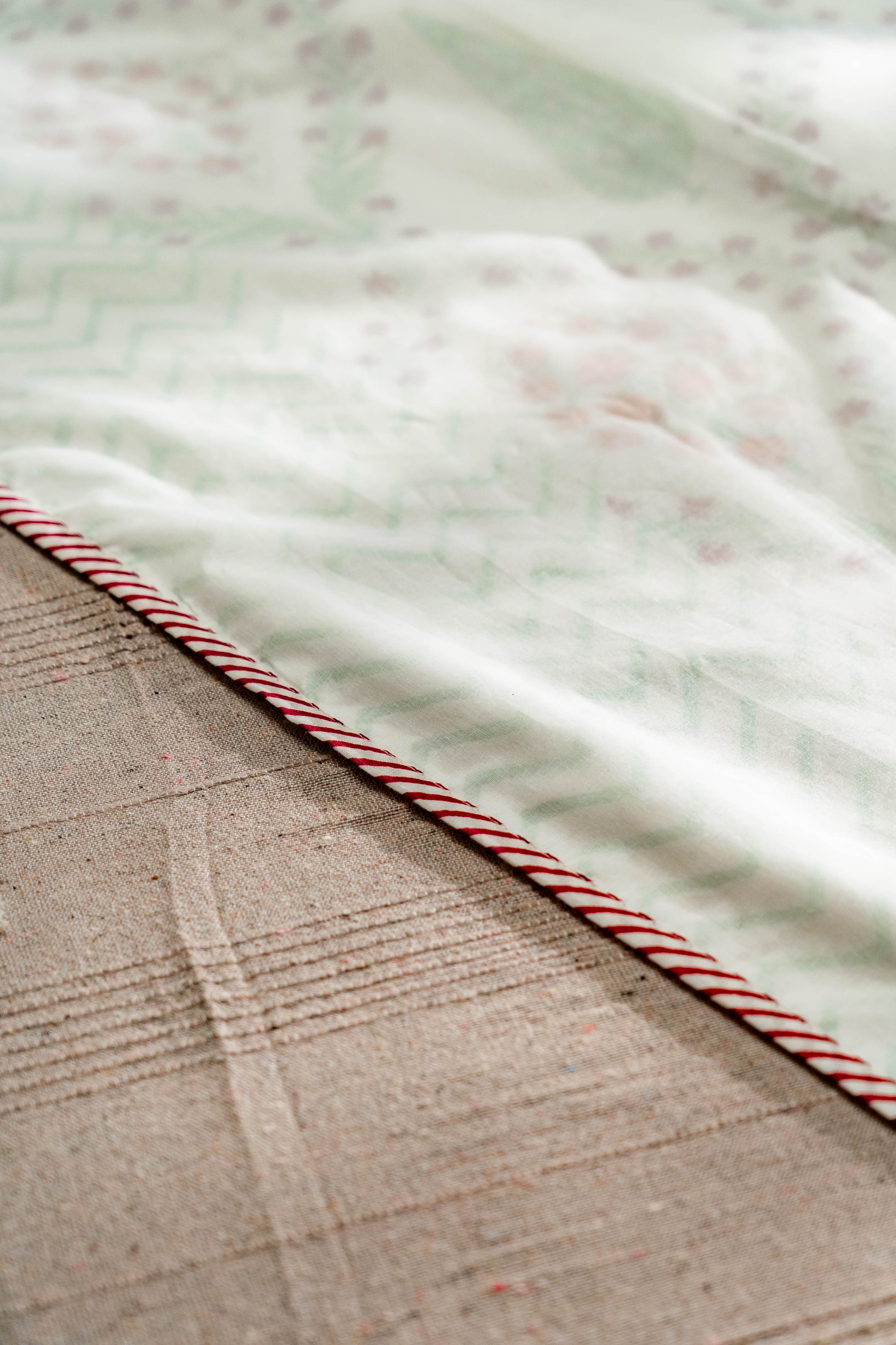 Three layers of fine muslin are stitched together in which the middle layer is hand block printed and edged with a striped flange.