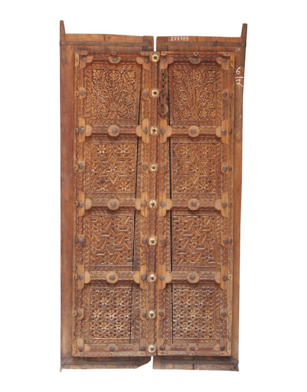 An antique carved wooden door with intricate geometric and floral patterns, featuring brass studs and hinges, shown against a plain white background.