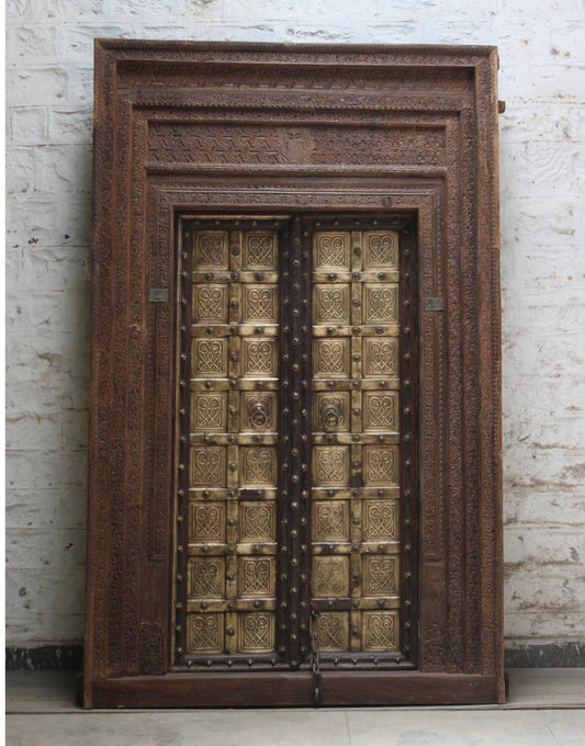 Decorative wooden door with intricate carvings against a white brick wall.