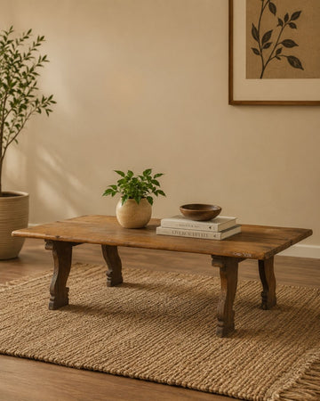 Wooden coffee table with decorative items in a room with a plant and framed artwork on the wall.
