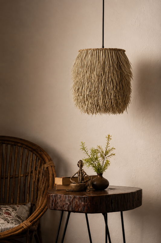 A bohemian-style woven straw pendant lamp hanging over a rustic wood side table with a small plant and decorative figurine, next to a wicker chair against a warm beige wall.