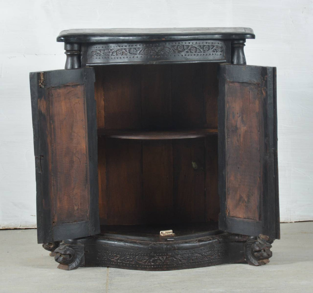 An antique carved wooden display cabinet with dark painted outer panels and open doors showing a warm brown interior, photographed against a plain light background.