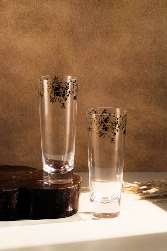 Two tall glasses with floral patterns on a wooden surface against a brown background