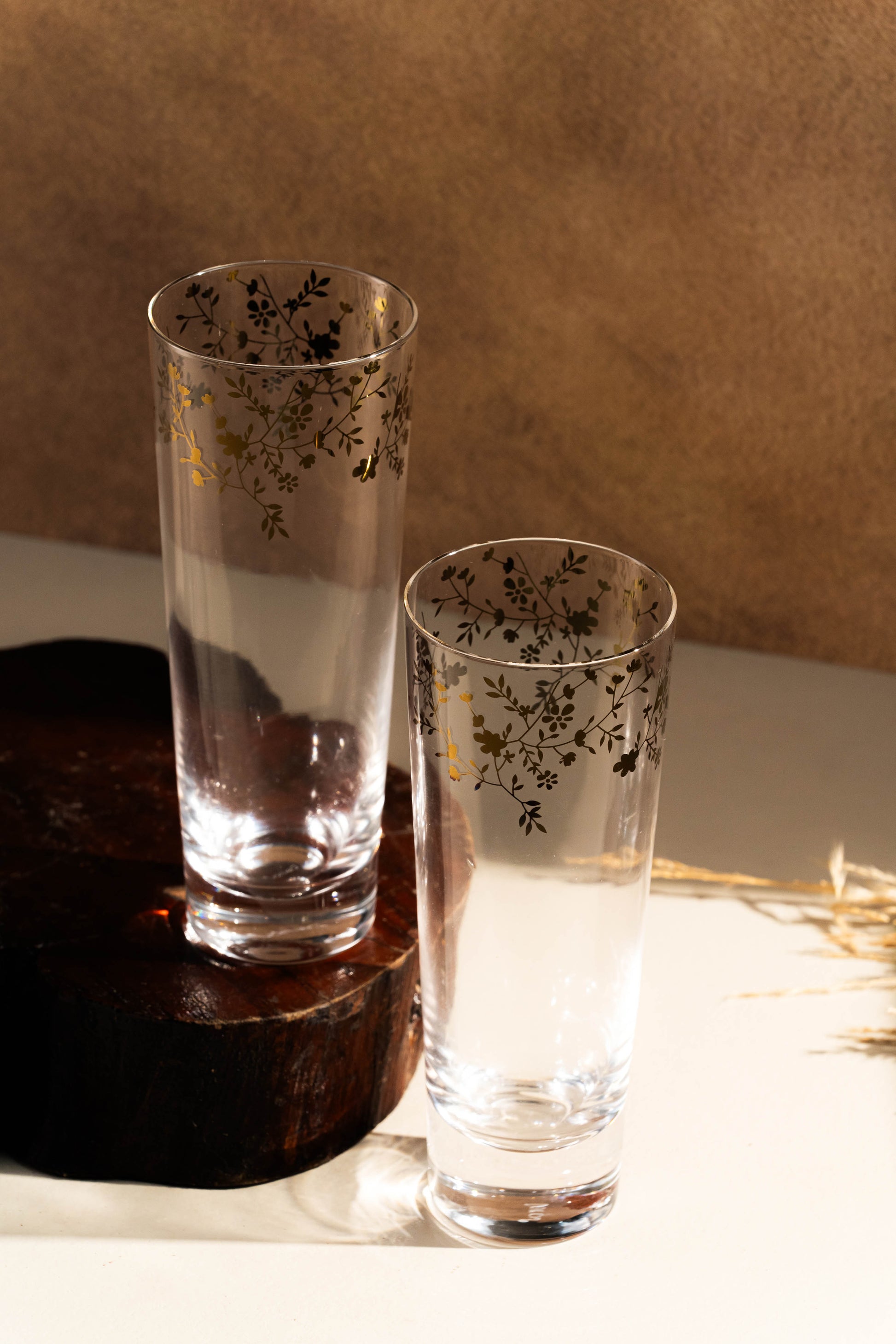 Two floral-patterned glasses on a wooden stand with a neutral background