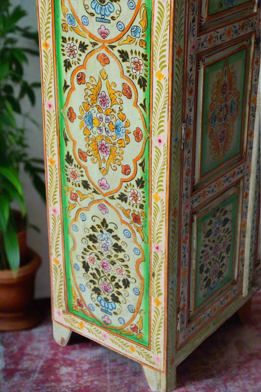 Decorative wooden cabinet with intricate floral patterns against a white brick wall.