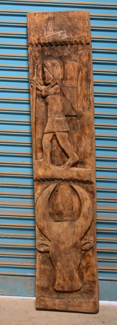 Wooden panel with carvings of a figure and an animal against a blue metal shutter background