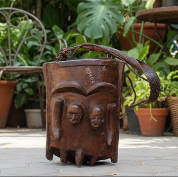 Rustic metal bucket with decorative carvings on a stone pavement