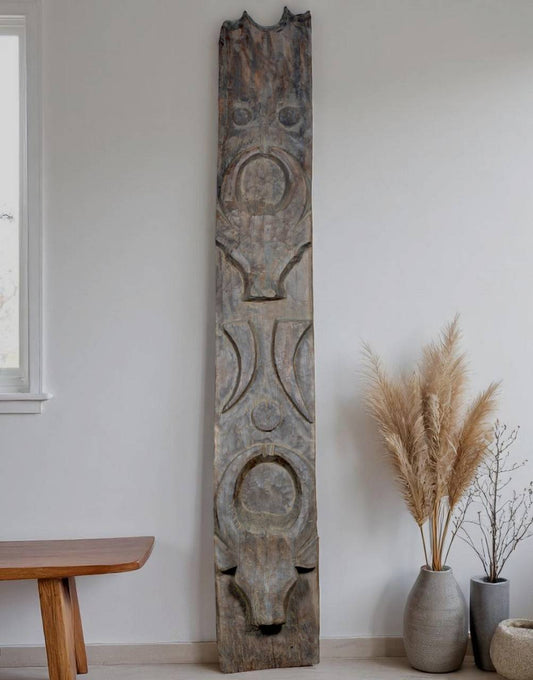 Tall wooden sculpture with carvings in a room with a table and decorative plants.