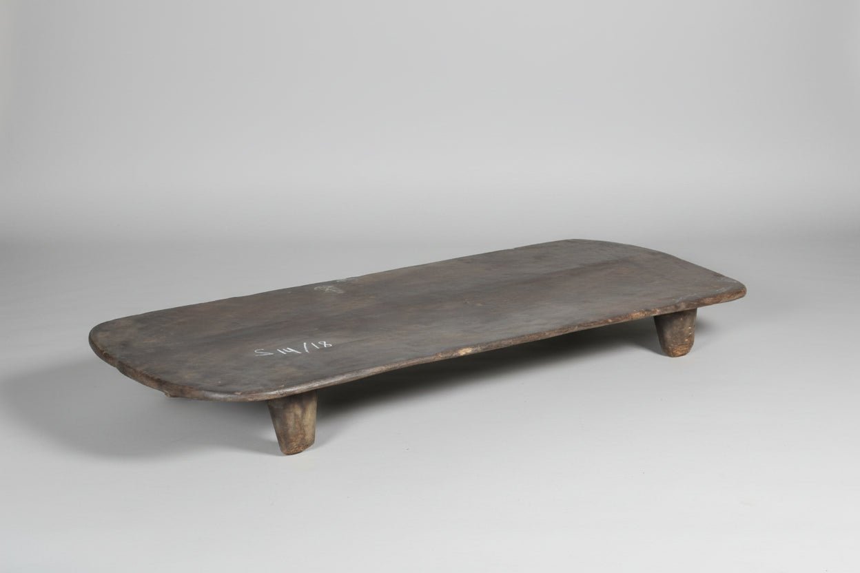 Long, narrow wooden table with rustic legs on a concrete floor.