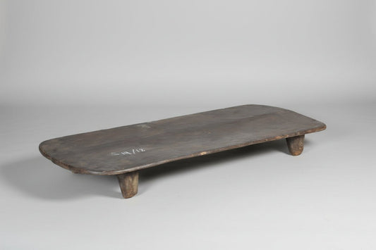 Long, narrow wooden table with rustic legs on a concrete floor.
