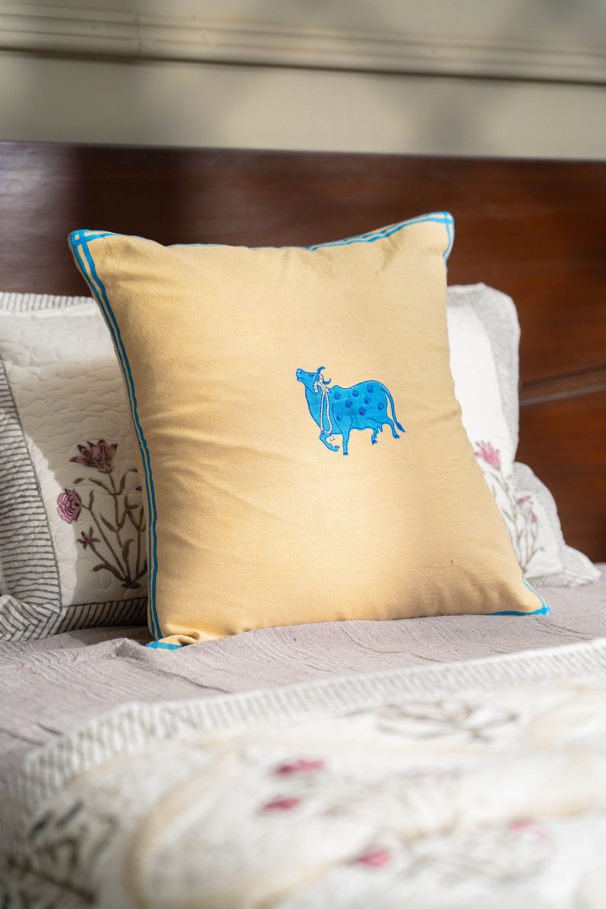 Yellow pillow with blue cow design on a bed with floral patterns