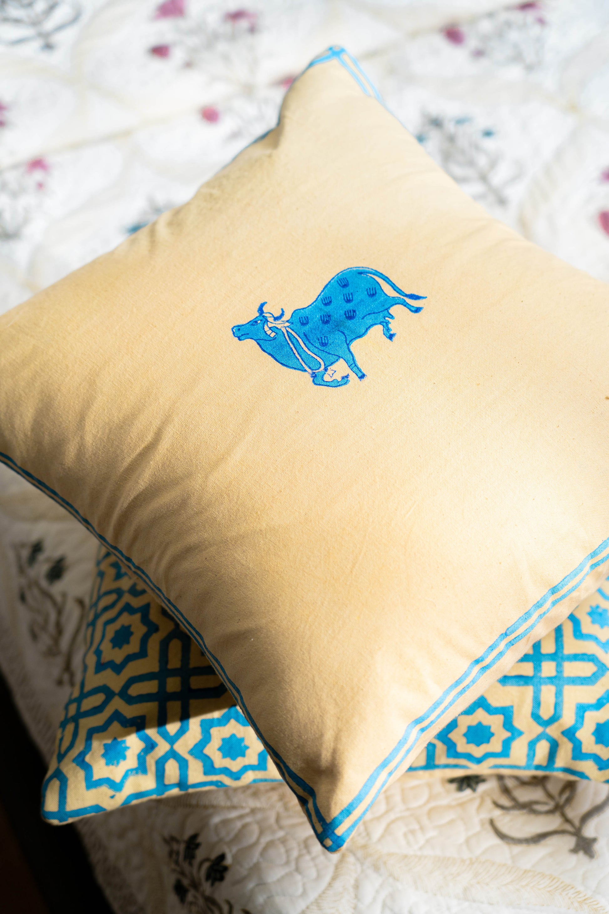 Beige pillow with blue decorative pattern on a floral bedspread