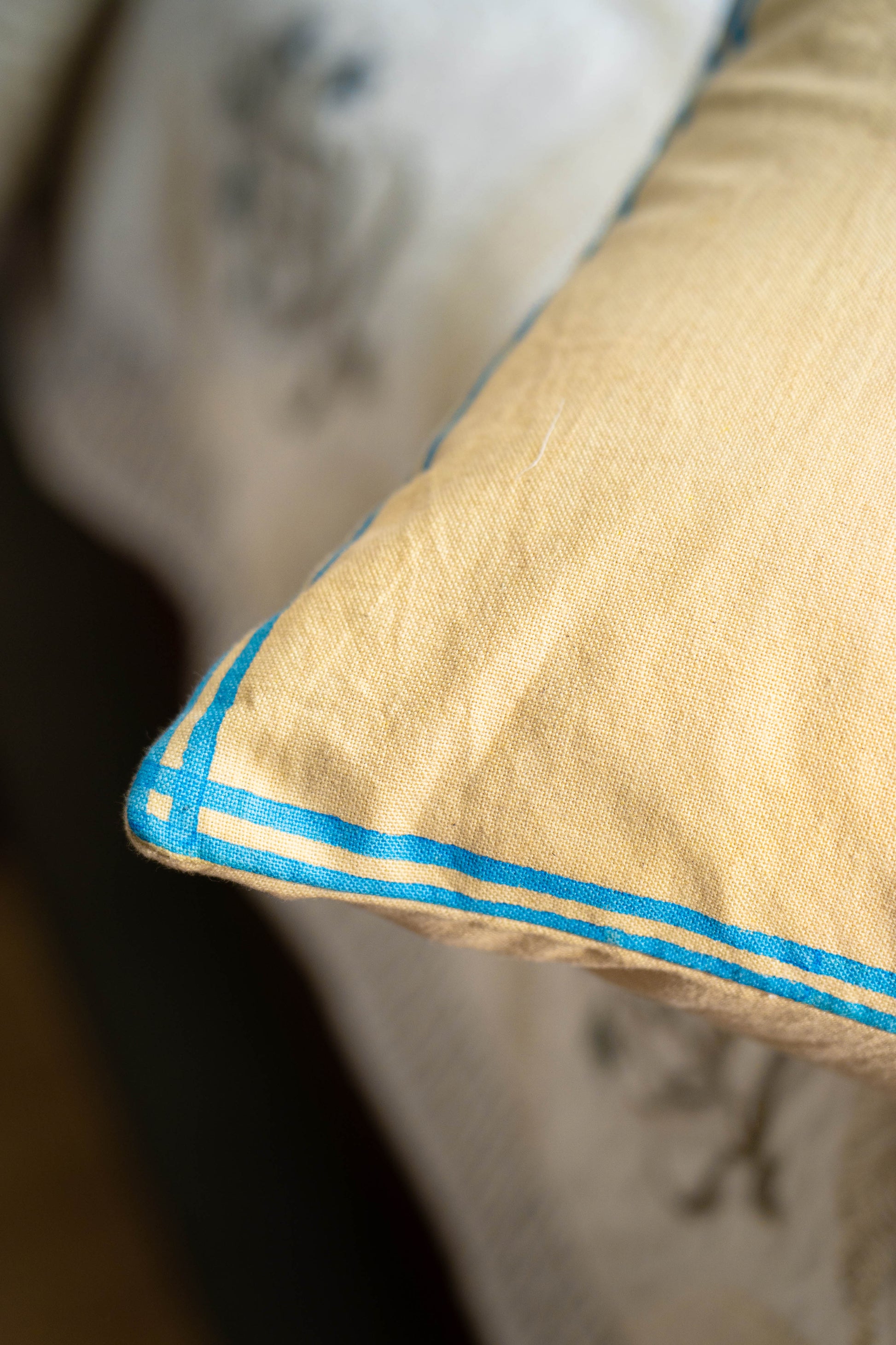 Beige pillow with blue stitching on a floral-patterned bedspread