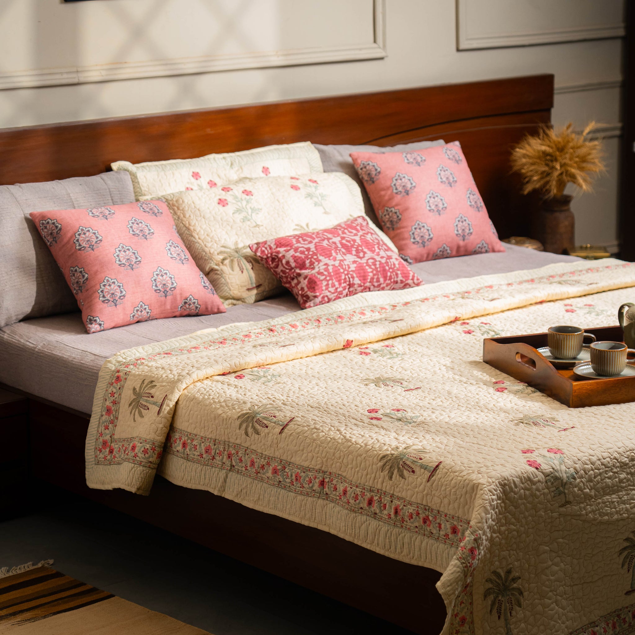 Bedroom with a bed featuring floral pillows and a decorative blanket, with a tray of cups on a nightstand.