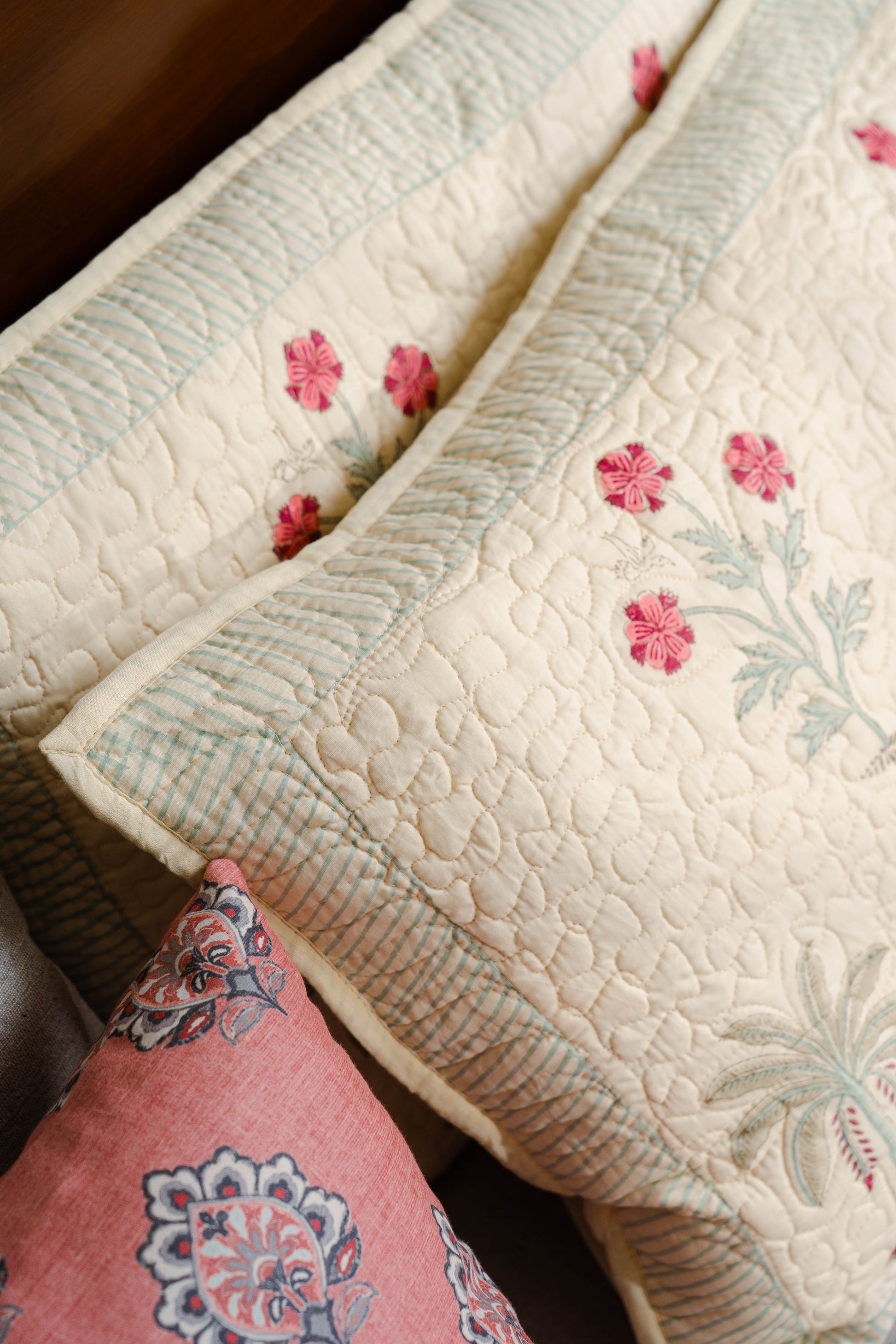 Close-up of a quilt with floral embroidery and a pink pillow.