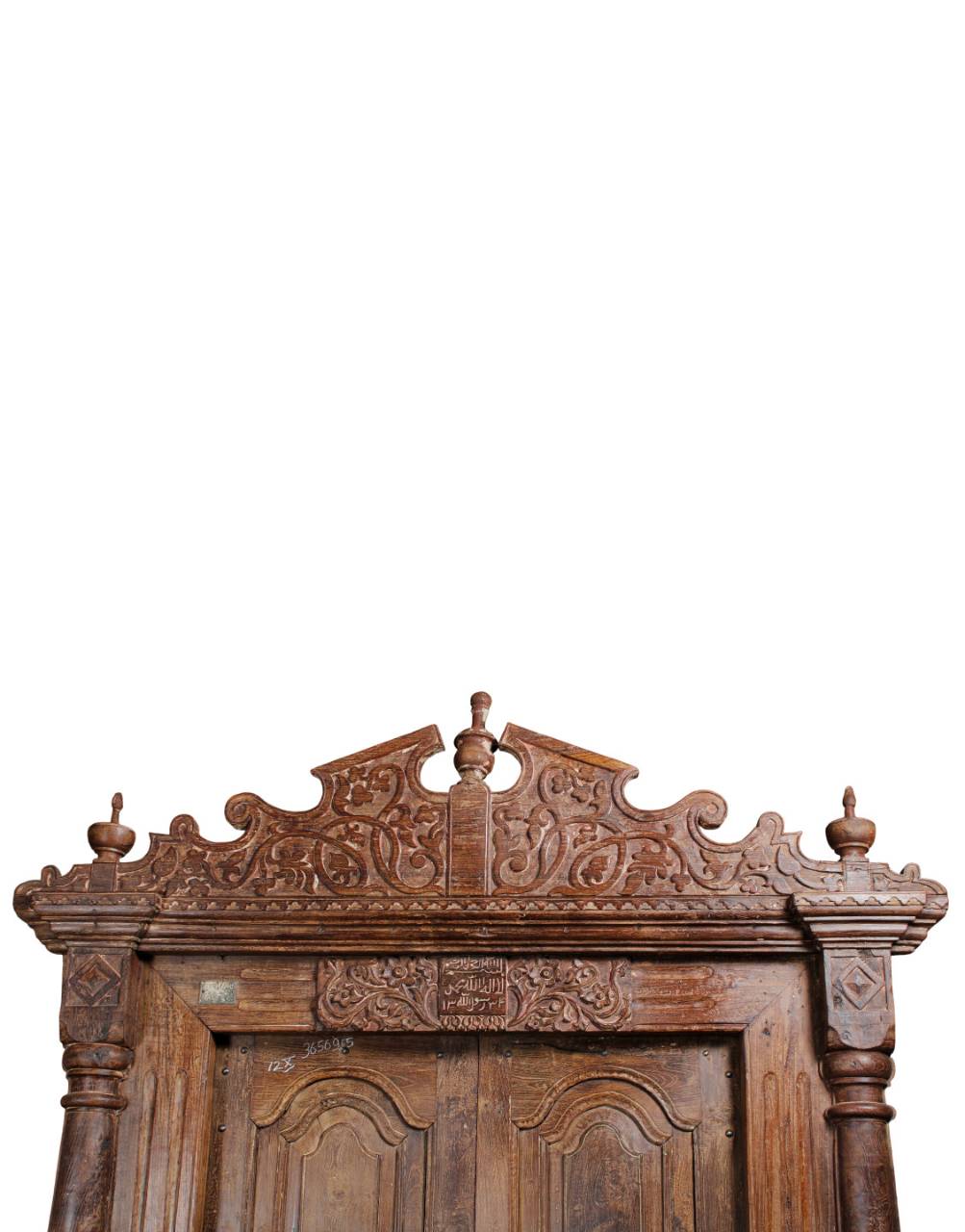 Close-up of an ornate carved wooden headboard or cabinet top with decorative scrollwork and turned finials, shown against a plain white background.