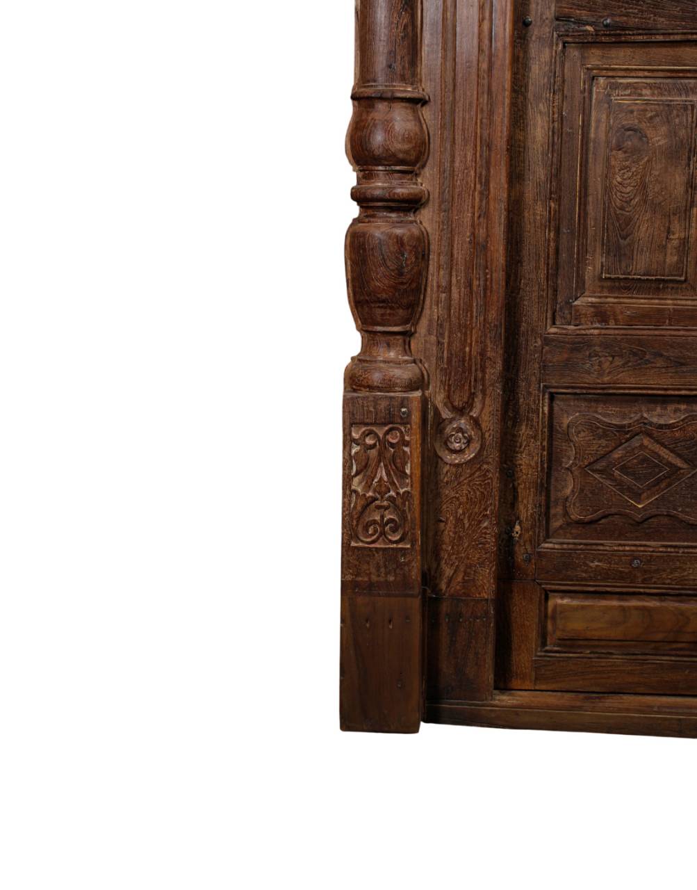 Close-up of an antique dark brown carved wooden door corner with ornate relief carvings and a turned post, shown against a plain white background.