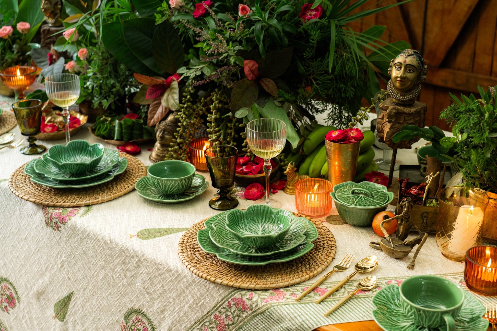 Decorative table setting with green ceramic plates, wine glasses, and candles on a floral tablecloth.
