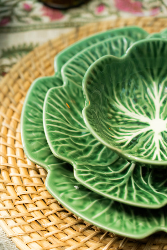 Stack of green ceramic plates with leaf pattern on a woven mat