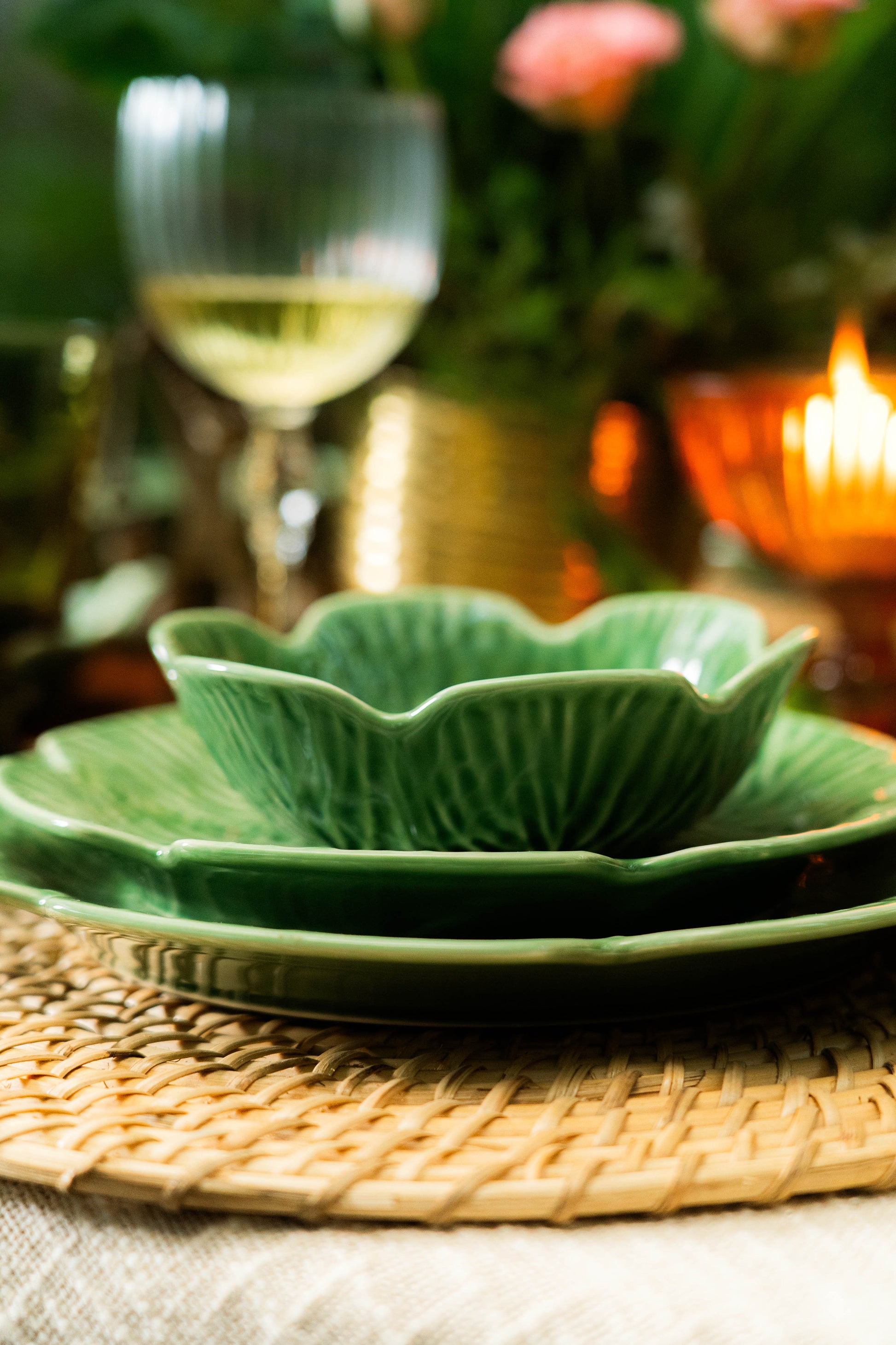 Green ceramic bowl and plate set on a woven placemat with a blurred background of a candle and glass.