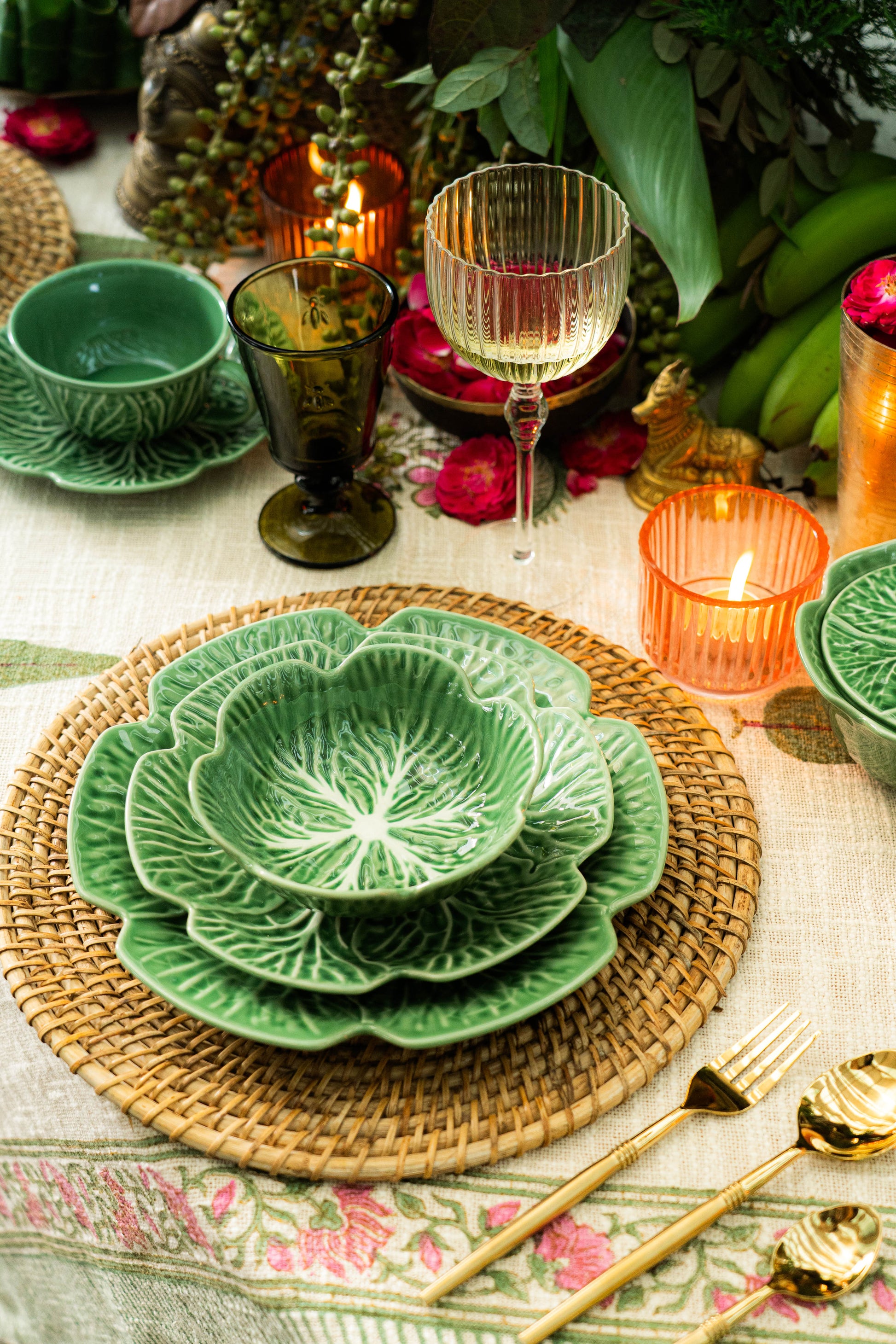 Decorative table setting with green ceramic plates, gold cutlery, and candles on a floral tablecloth.