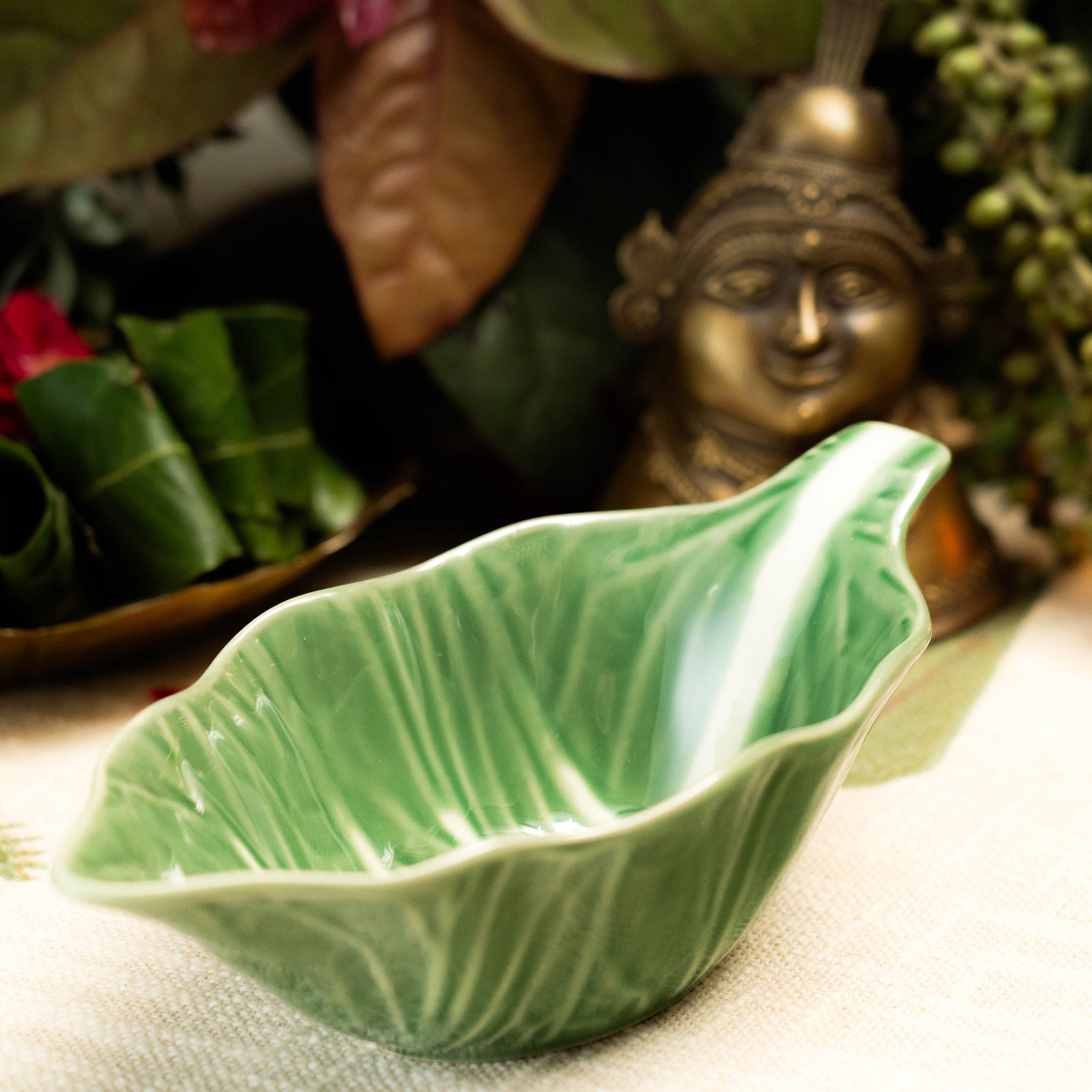 Green ceramic leaf-shaped bowl on a textured surface with decorative elements in the background