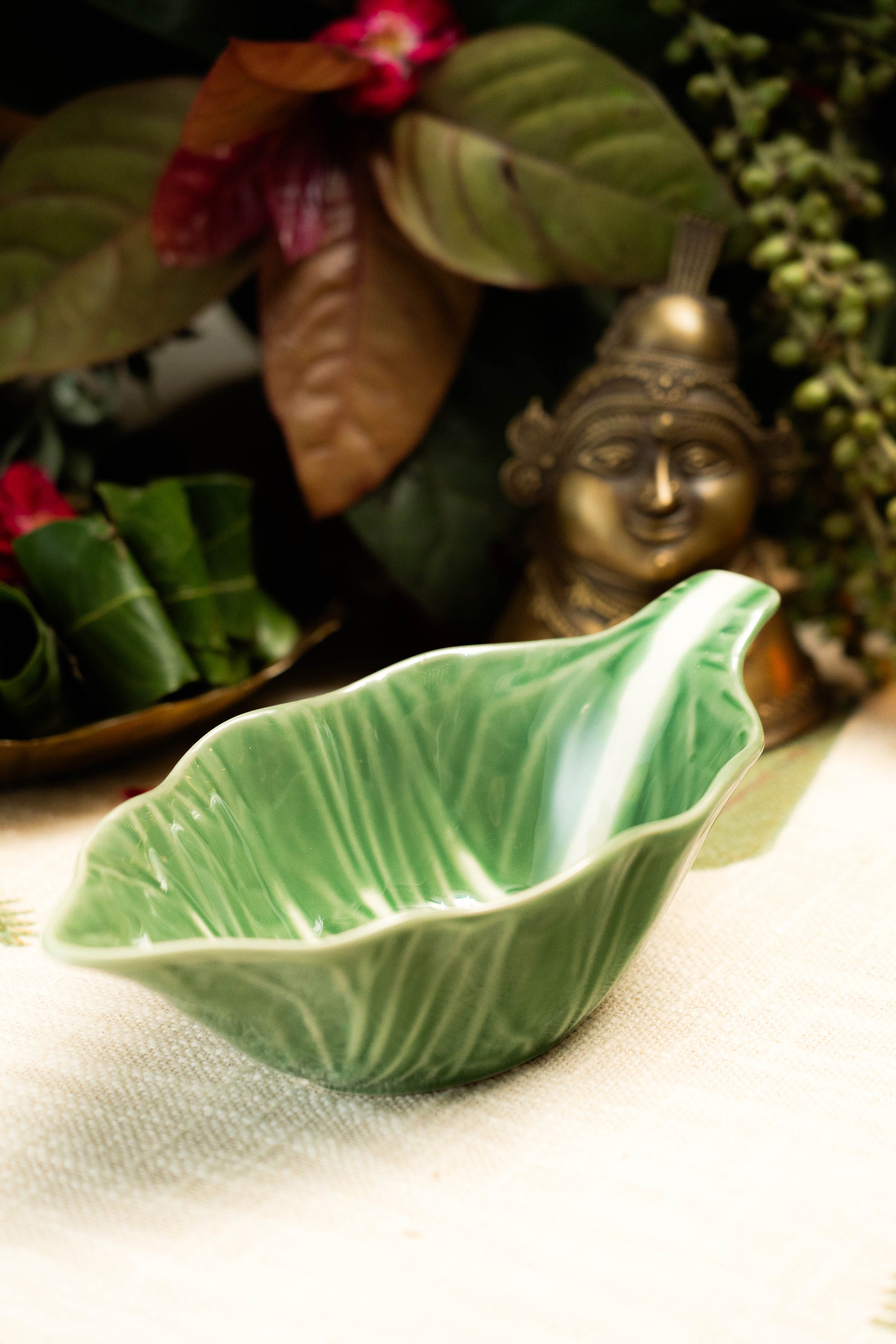 Green ceramic leaf-shaped bowl on a textured surface with decorative elements in the background