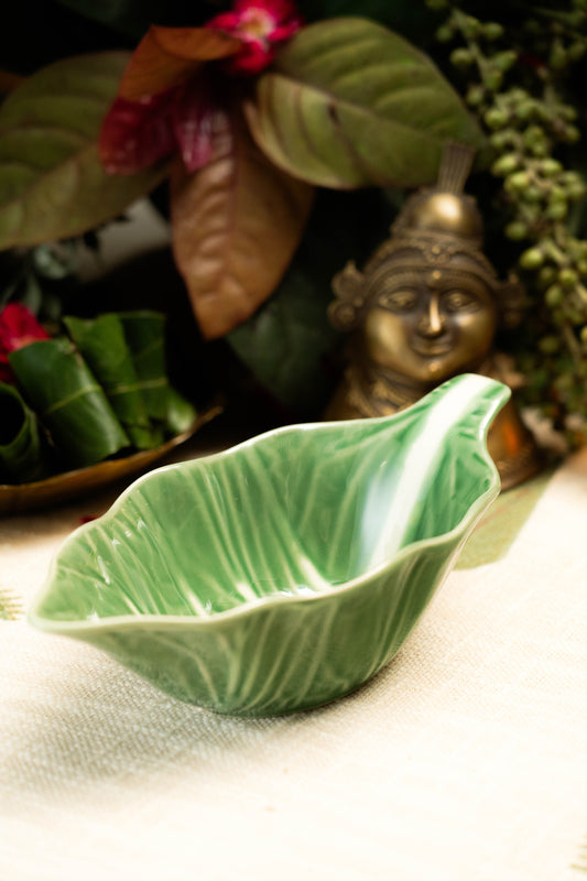 Green ceramic leaf-shaped bowl on a textured surface with decorative elements in the background