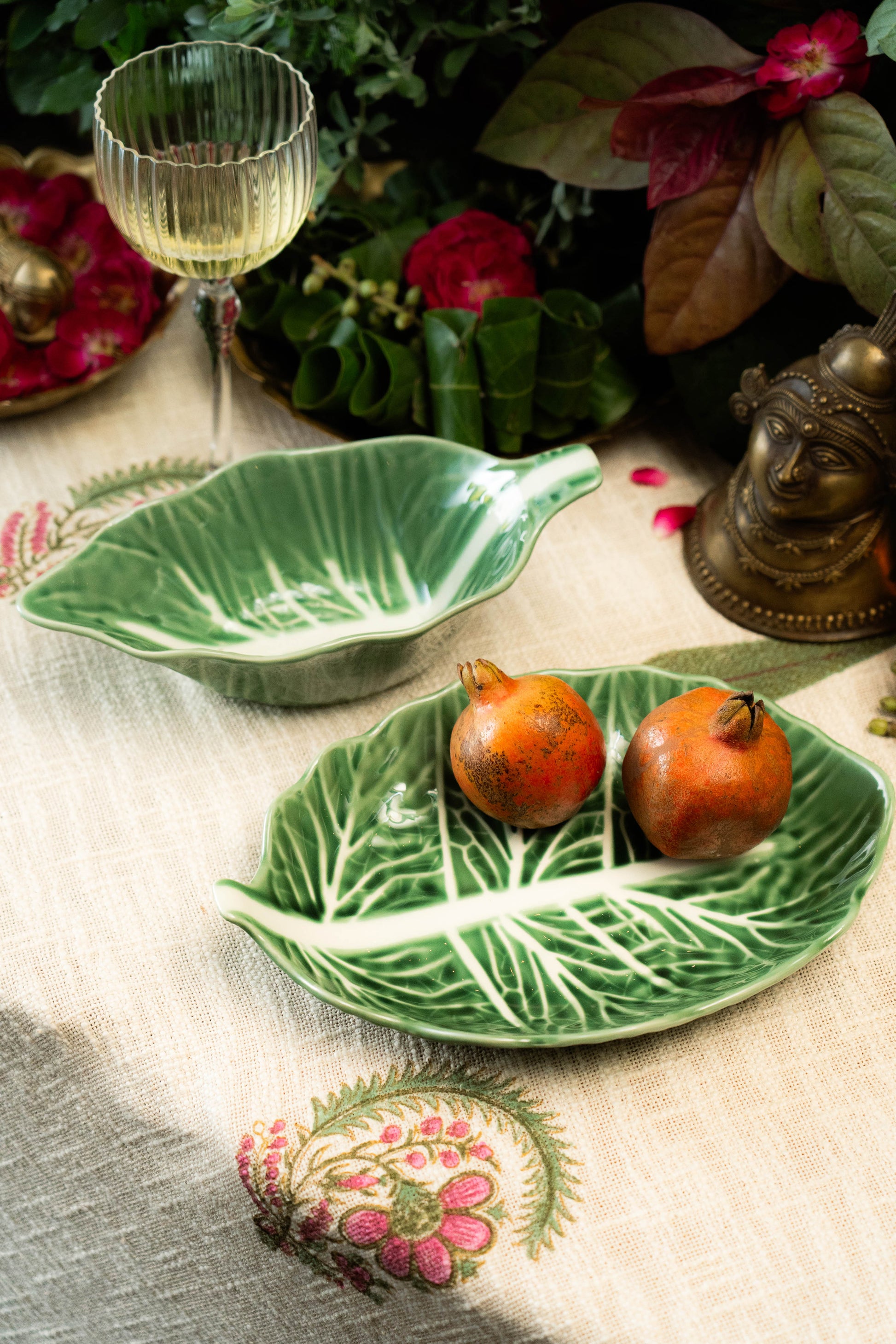 Green leaf-shaped dish with pomegranates on a decorative table setting with flowers and a candle.