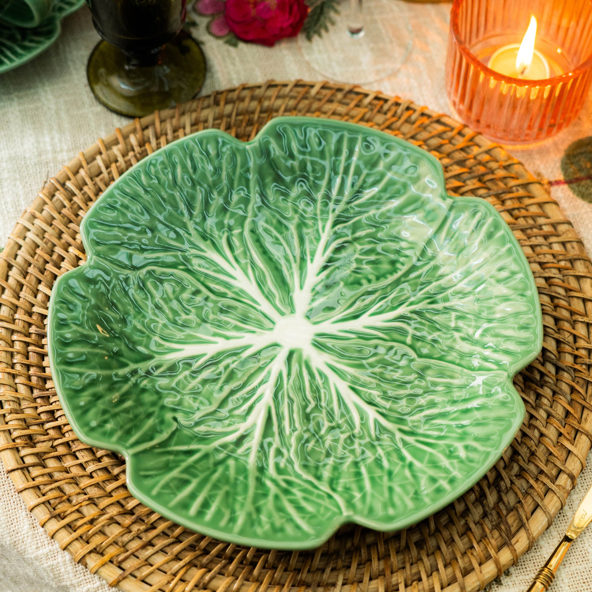 Green leaf-shaped ceramic plate on a woven placemat with candles and flowers in the background.