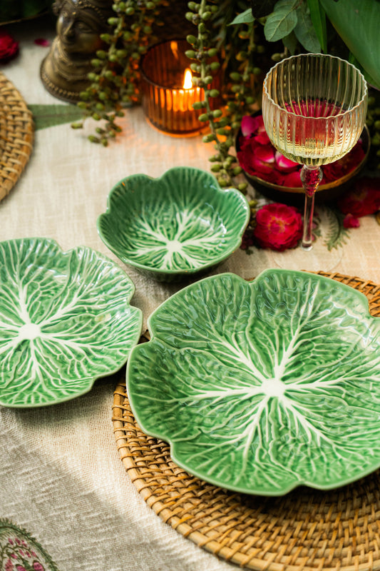 Green leaf-patterned ceramic plates on a textured surface with candles and flowers in the background.