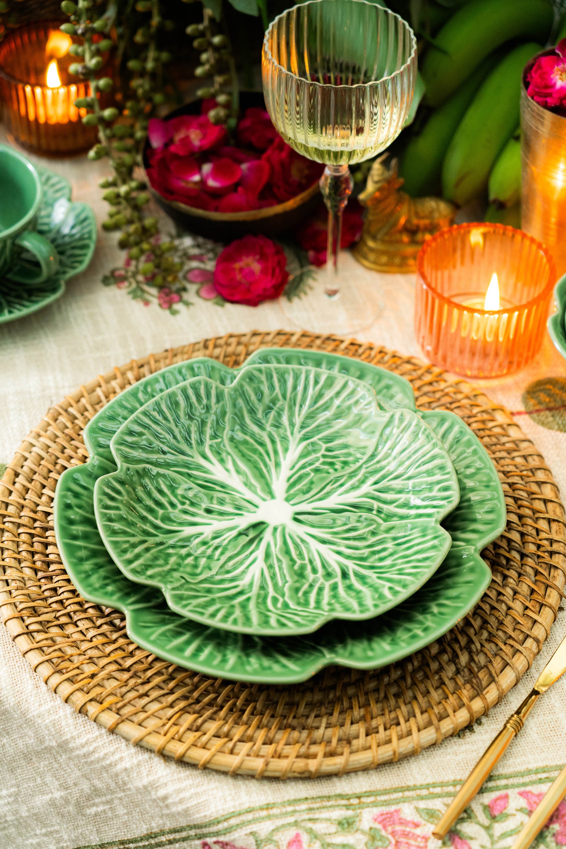 Green ceramic leaf-shaped plate on a woven placemat with candles and flowers in the background