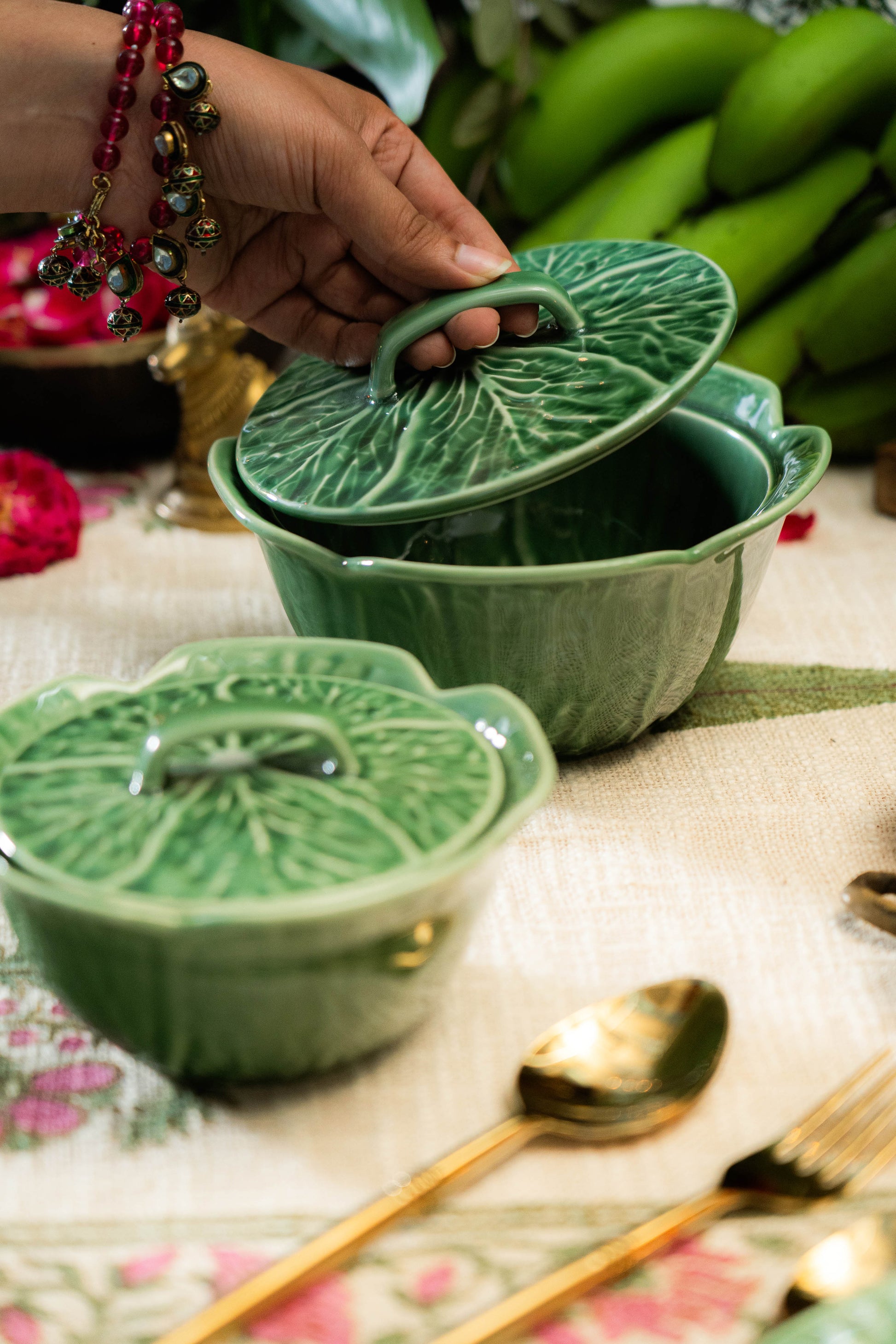 Green ceramic dishes with leaf designs on a floral tablecloth.