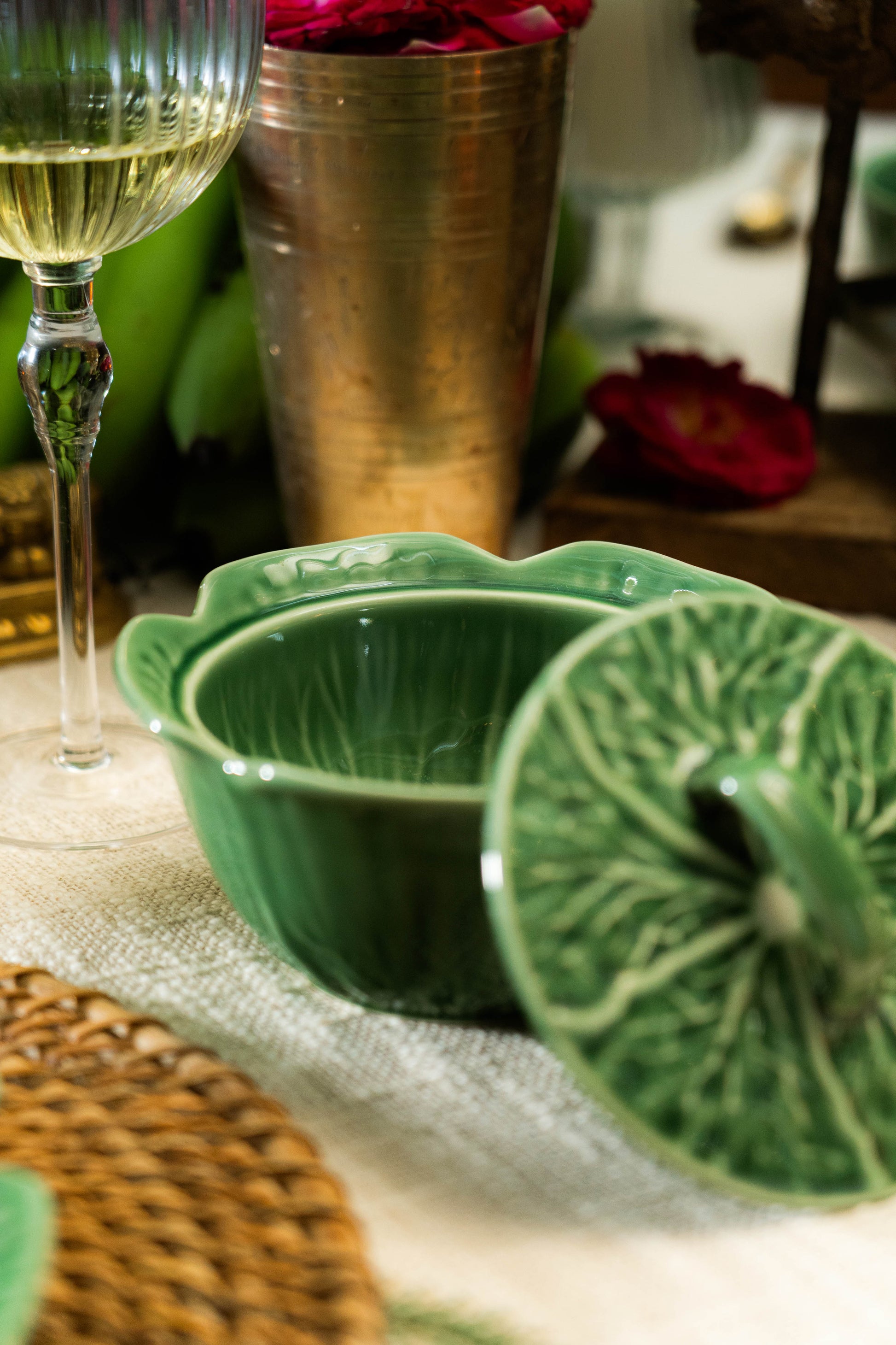 Green ceramic dish with lid on a table with a glass of white wine and a metallic container.