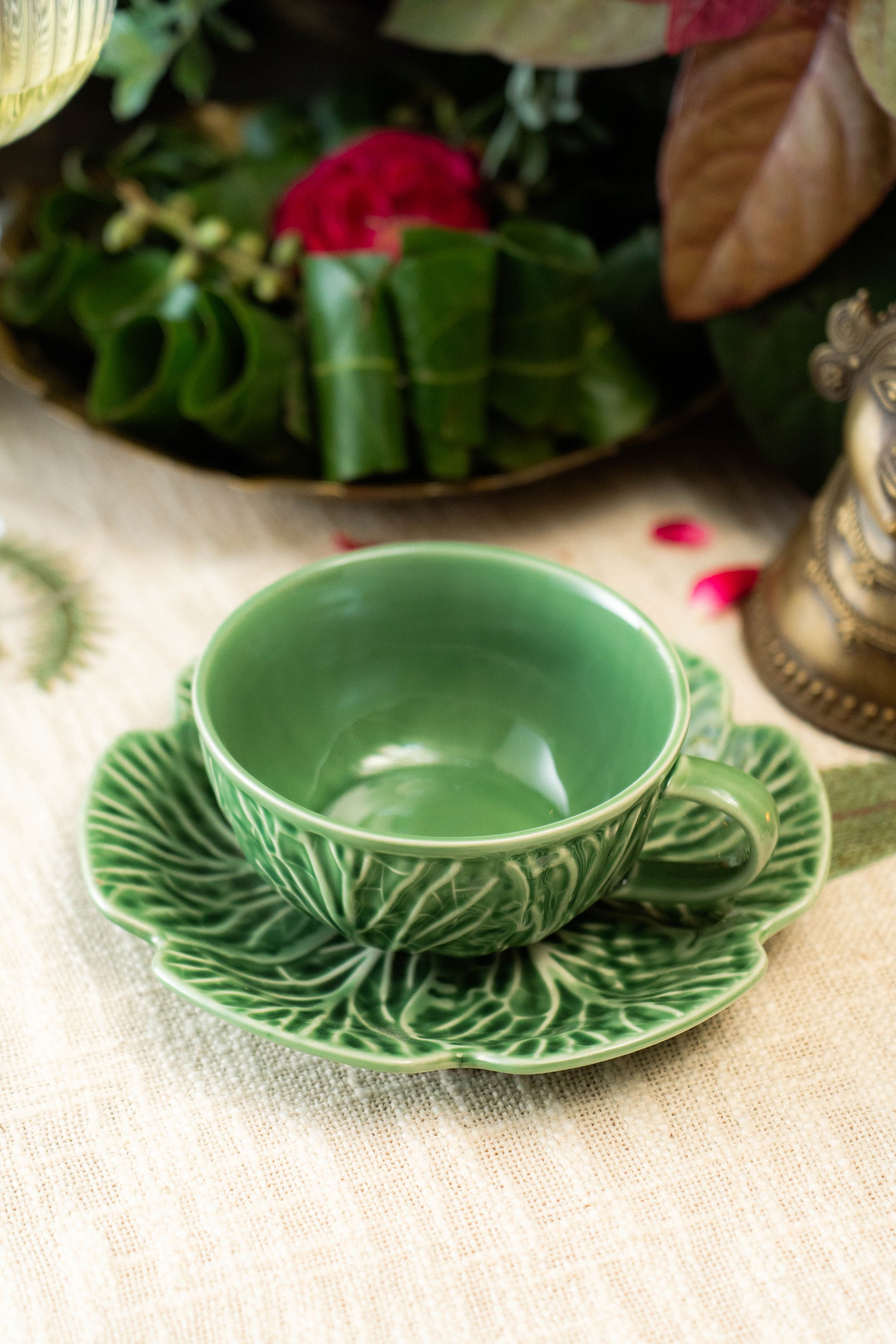 Green ceramic teacup and saucer on a textured surface with floral decorations in the background.