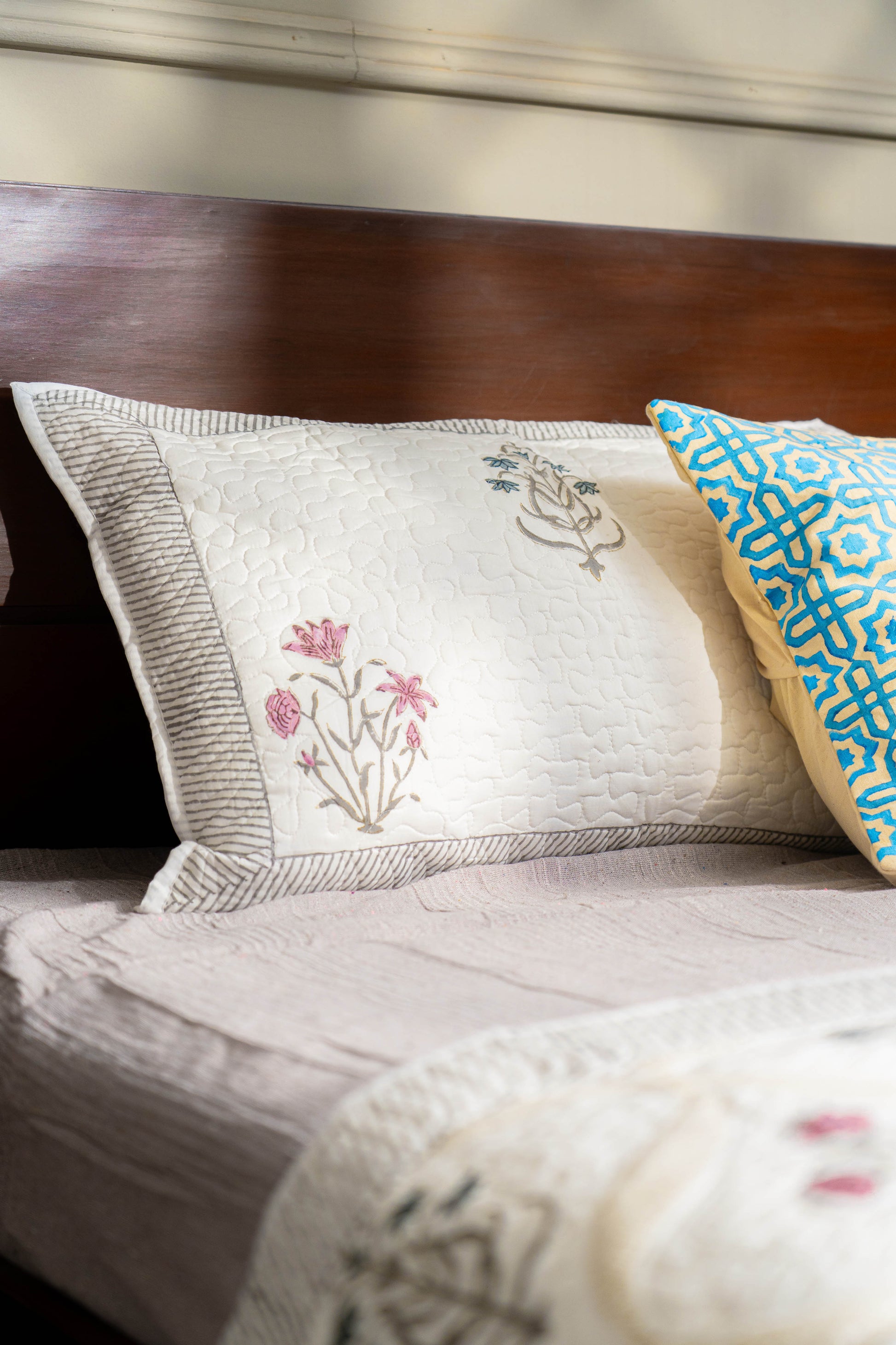 Decorative pillows with floral embroidery and geometric pattern on a bed.