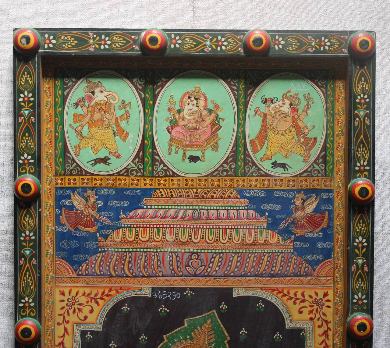 A framed traditional Indian hand-painted woodblock print (Kakudi) depicting Lord Ganesha, featuring three oval panels at the top, a central temple structure, and an ornate decorated border.