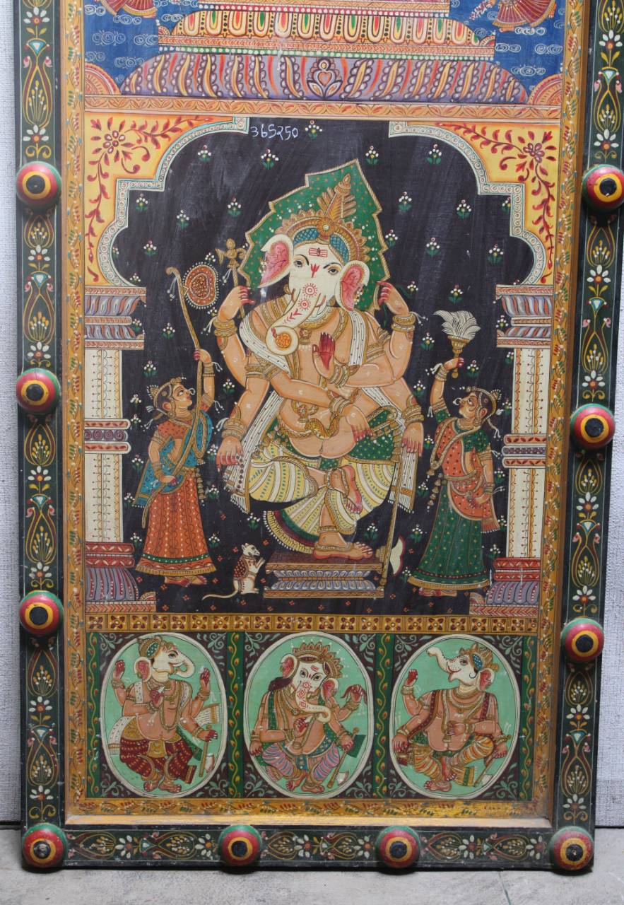 A traditional Indian hand-painted wooden panel featuring Lord Ganesha, with three oval panels at the bottom and decorative corner finials, photographed against a neutral gray background.