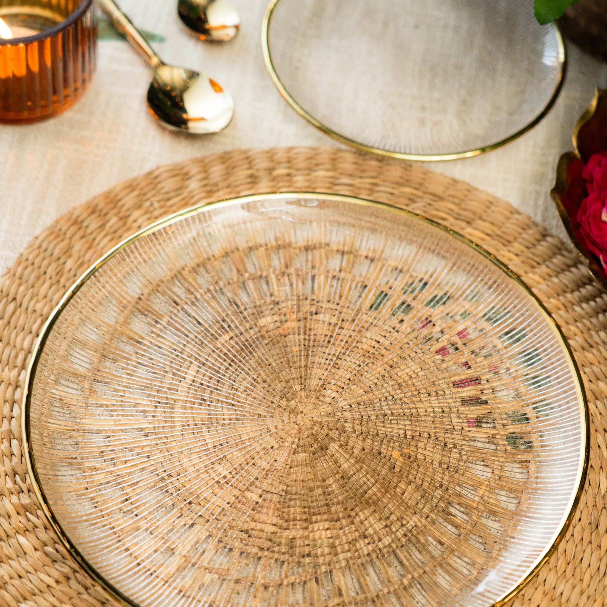 Woven placemat with gold rim on a table setting with glasses and cutlery.